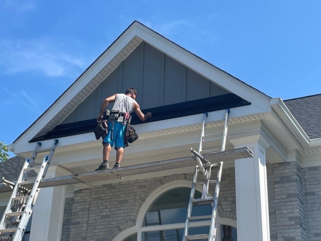 Porter Family Exteriors contractor installing a black metal roof accent above the home&rsquo;s front entrance