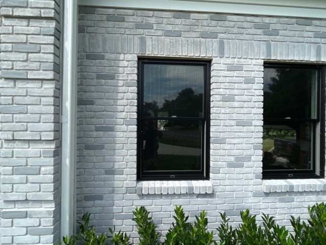 Black replacement windows installed by Porter Family Exteriors within the home&rsquo;s white brick exterior