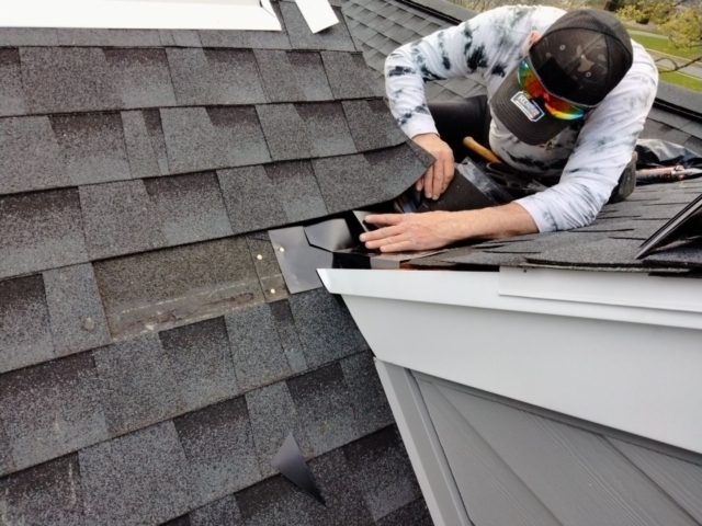 Close-up of a Porter Family Exteriors roofer fitting metal flashing beneath asphalt roof shingles
